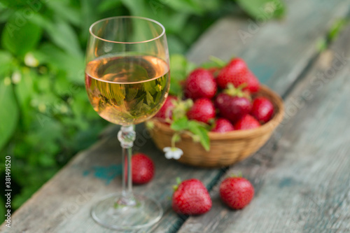 Glass of rose wine served with fresh strawberries on wooden background. Picnic outdoor with pink wine and berries.