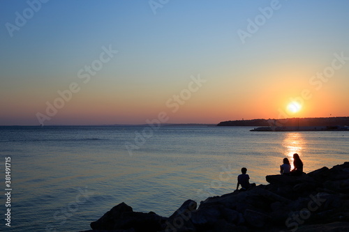 Fototapeta Naklejka Na Ścianę i Meble -  A sunset on the beach. Silivri, Turkey. Young people chatting on the cliffs on the beach at a calm sunset.