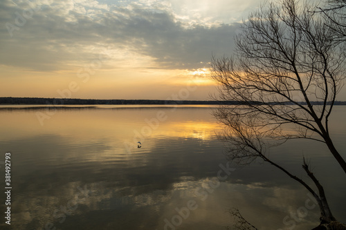 Moody evening lake landscape with sunset over water edge and sky reflecting in the water.