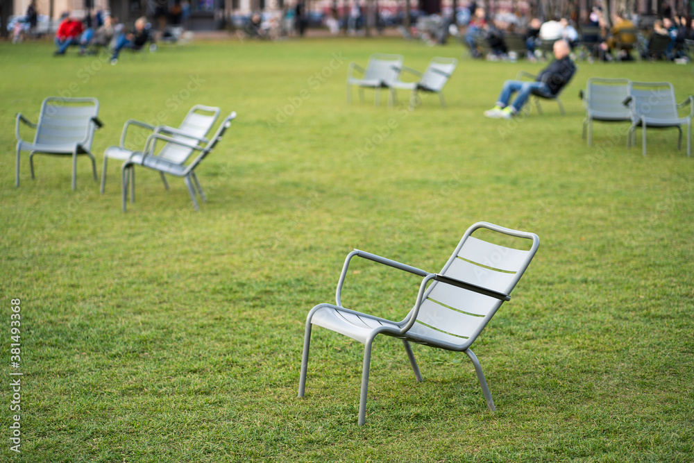 Green iron chairs on green lawn in empty public space. Autumn season. 