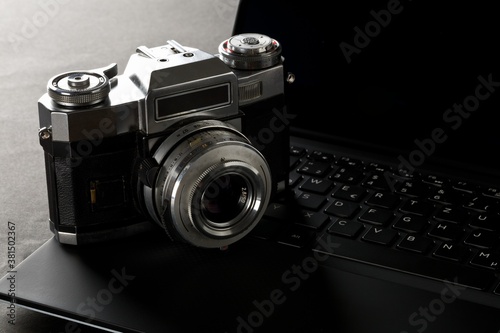 Retro analog SLR camera on laptop keyboard on black desk in office, digital photography or image processing concept