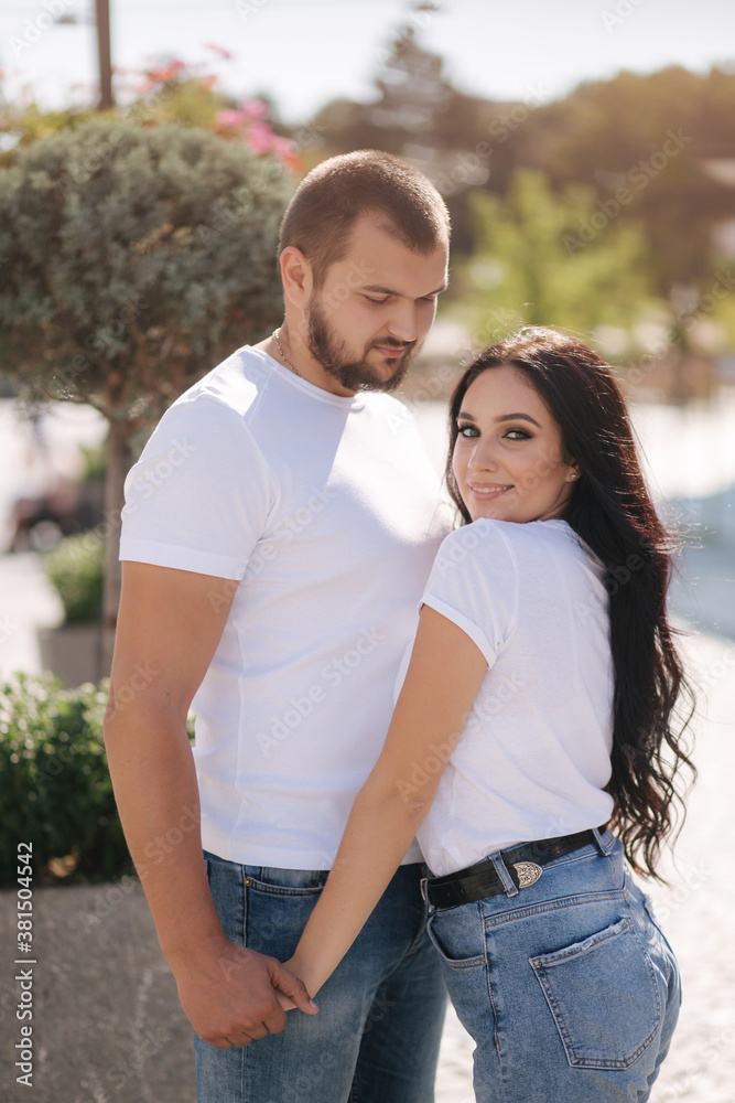 Stylish couple in denim and white t-shirts stand in centre of the city. Late summer concept