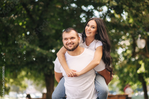 Beautiful gilr climbed on her boyfriend back and hug him. Happy smiled couple spend time in city