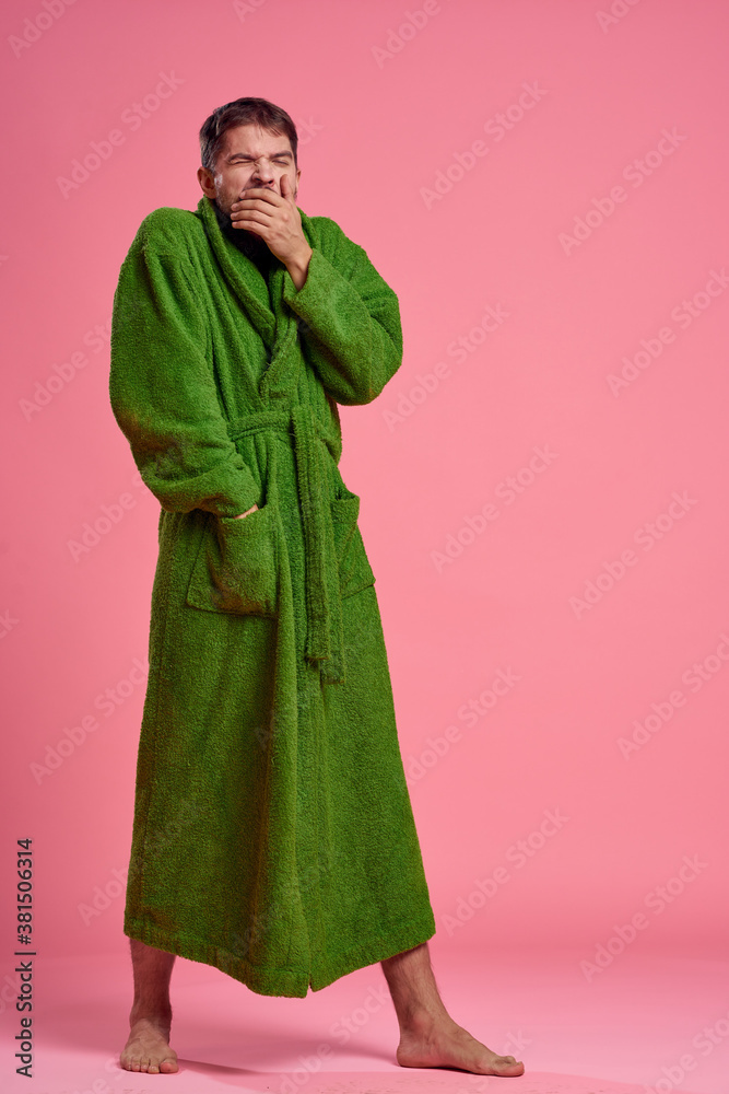 An emotional man in a green robe in full growth on a pink background gestures with his hands to the model