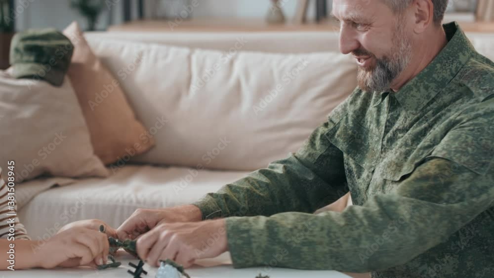 Slowmo tracking of happy bearded male army officer in uniform and his son playing with toy soldiers in living room Slowmo tracking of happy bearded male army officer in uniform and his son playing with toy soldiers in living room