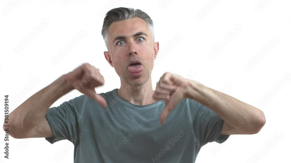 Funny middle-aged guy with grey hair and bristle, complaining over something bad or boring, showing thumbs-down in dislike, stick tongue and roll eyes, standing over white background Funny middle-aged guy with grey hair and bristle, complaining over something bad or boring, showing thumbs-down in dislike, stick tongue and roll eyes, standing over white background