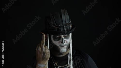 Sinister man with skull makeup making faces and showing middle finger. Bad manner gesture. Halloween