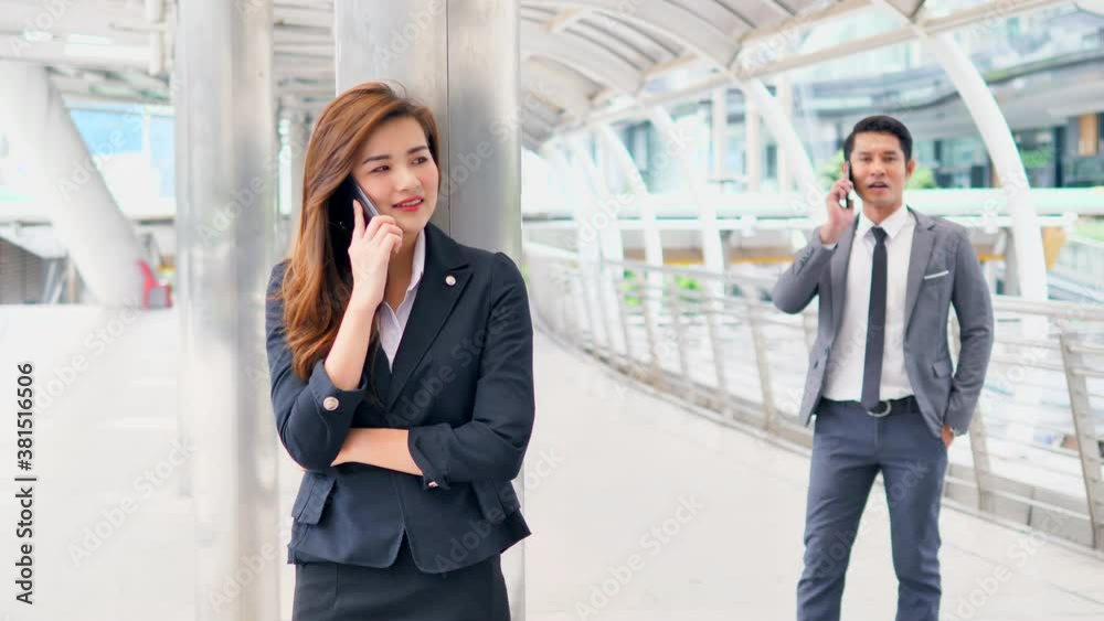 Two Businesspeople with Smartphone near office. Beautiful smiling female and handsome asian man in fashion office clothes talking on phone while standing outdoors. Phone communication. Two Businesspeople with Smartphone near office. Beautiful smiling female and handsome asian man in fashion office clothes talking on phone while standing outdoors. Phone communication.