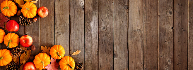Autumn corner border with pumpkins, leaves and apples. Top down view on a rustic dark wood background with copy space.