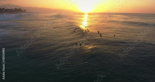 Sunset over group of surfers in Hawaii, wide aerial