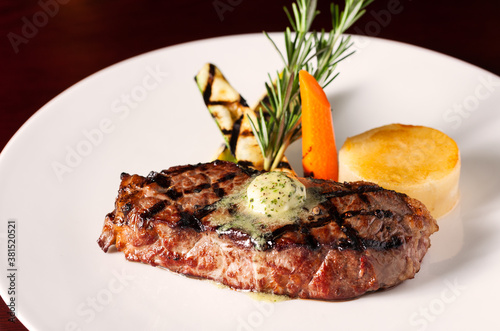 Gourmet boneless grilled rib-eye steak with herbed butter, carrot and potato with rosemary garnish; copy space