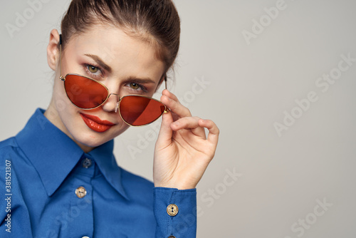 Fashionable woman in sunglasses and a blue shirt gesturing with her hands on a light background cropped view