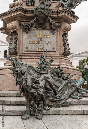 Quito, Ecuador - December 2, 2008: Historic downtown, Plaza Grande. Closeup of lion with flags and cross bronze statue at foot of Independence Monument, or Heroes of August 10.  photo