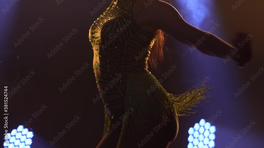 A slender female dancer moves her hips practicing the movements of the salsa dance. A woman in a shiny dress is moving in slow motion. Close up shot.