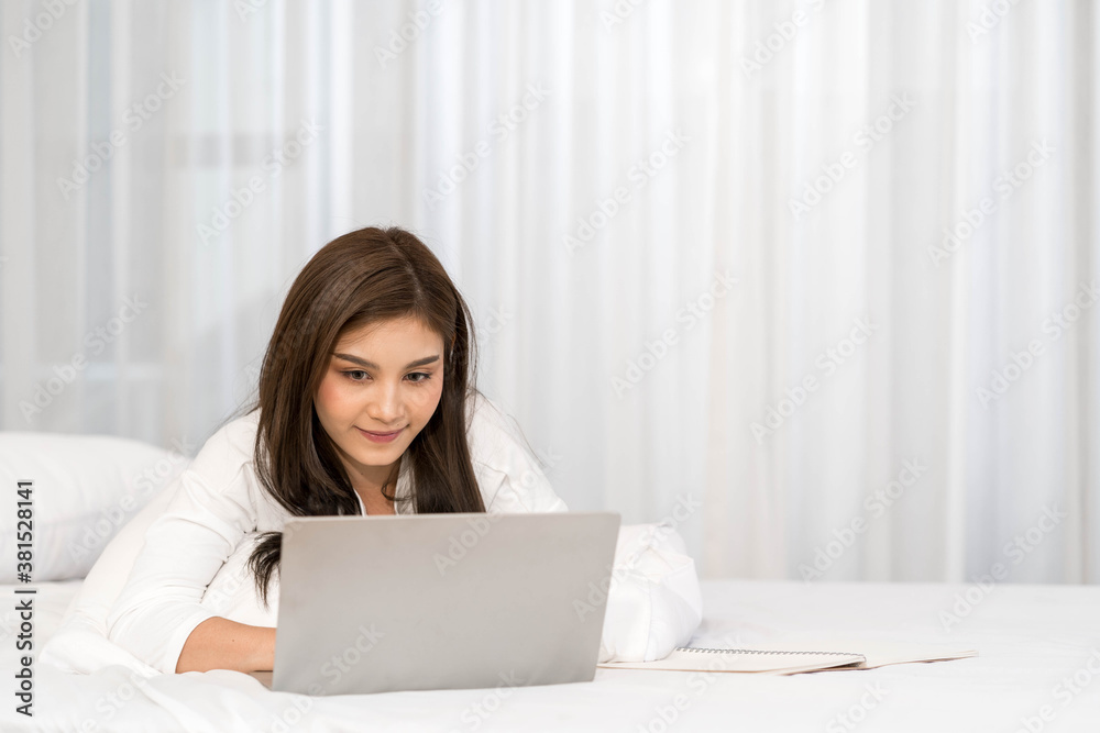Happy casual beautiful asian woman working on laptop computer while setting on the bed in the house. Happy casual beautiful asian woman working on laptop computer while setting on the bed in the house.
