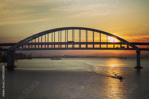 日の出に赤く染まる海と空。六甲大橋を通過する船も赤く染まる。橋の下には大阪湾、その向こうには生駒山系と高層ビルを望む。 © 宮岸孝守