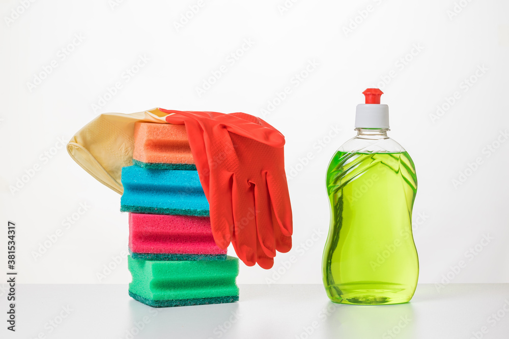 A set of foam sponges, dish washing gel and gloves on a white table. A set of foam sponges, dish washing gel and gloves on a white table.