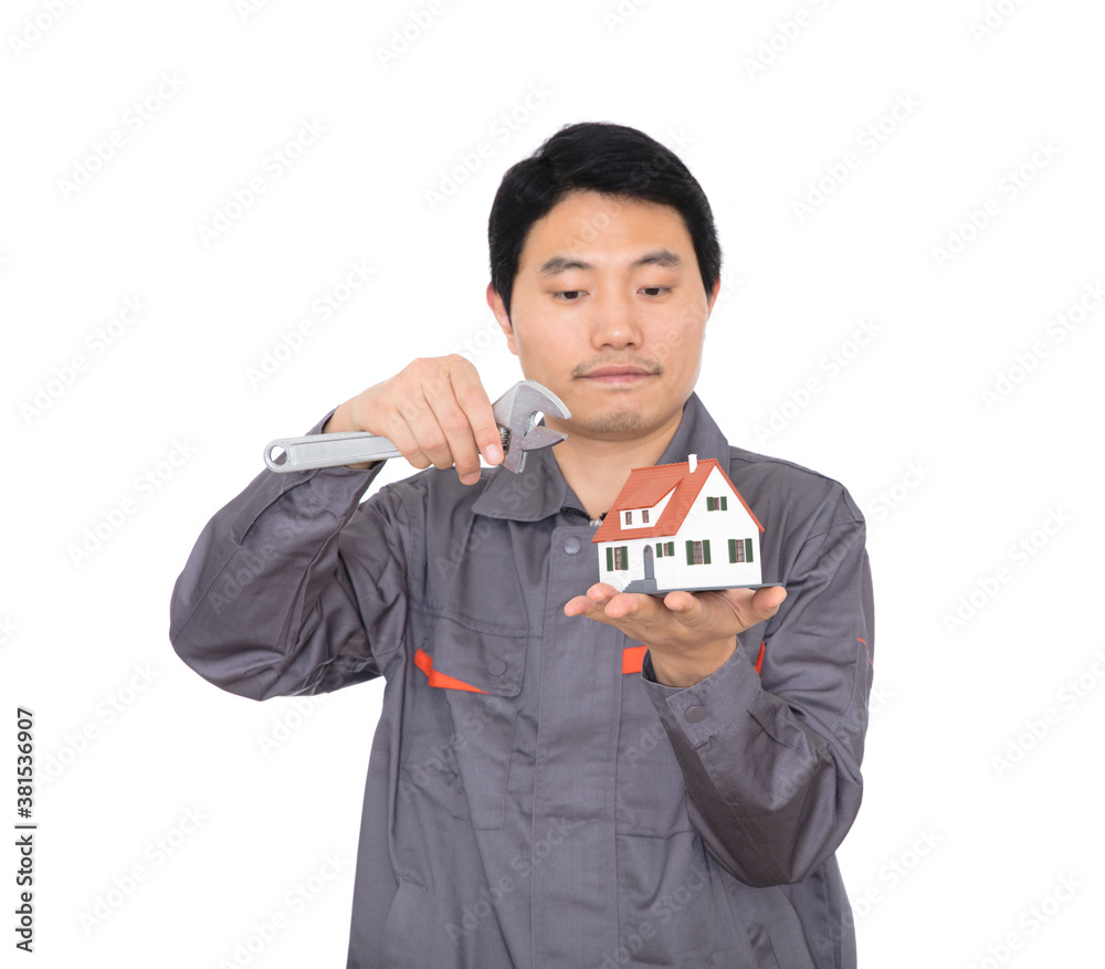 Young worker in front of white background holding a wrench in hand in front of the house model Young worker in front of white background holding a wrench in hand in front of the house model