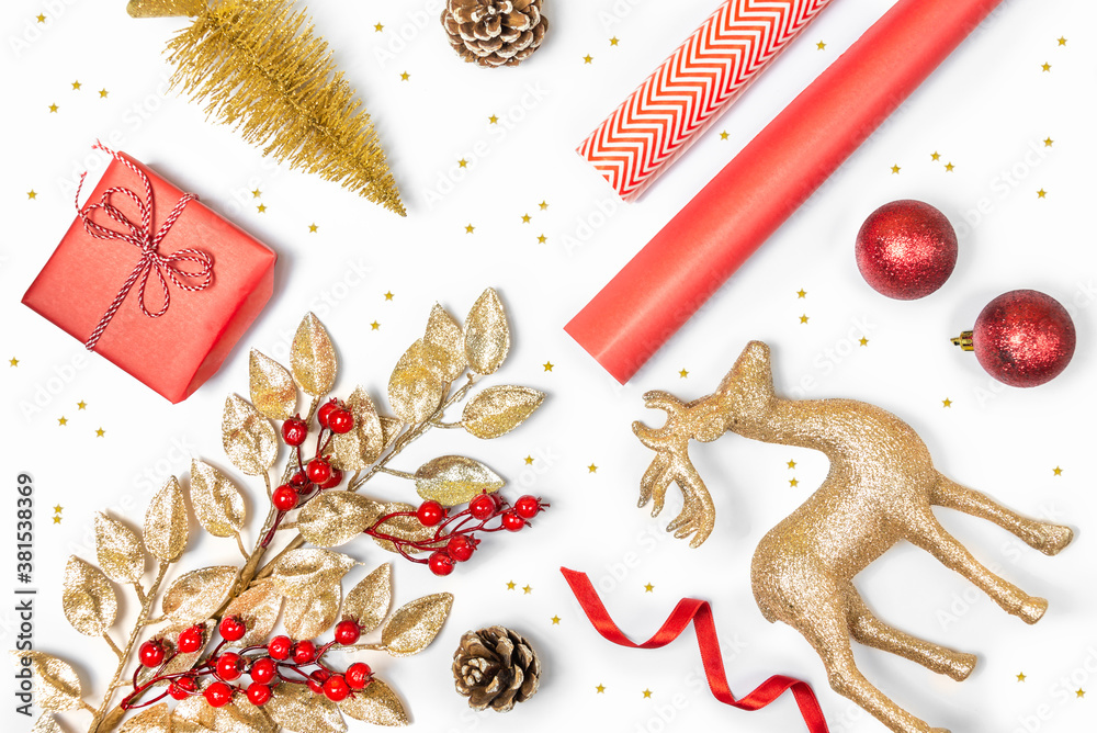 Christmas presents preparation - gift box, mistletoe, fircones,reindeer, christmas balls and paper in golden and red colors over white background.