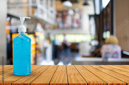 Hand sanitizer bottle on wooden table top in blurred coffee shop. Please wash your hands concept.