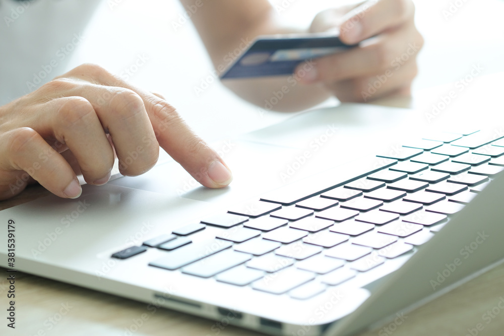 Young man sat in the living room on sofa , using his computer and holding credit card her online To buy product in the internet Young man sat in the living room on sofa , using his computer and holding credit card her online To buy product in the internet
