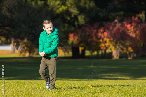 Сheerful boy walking on green field in park on a warm autumn day. The concept happy childhood.
