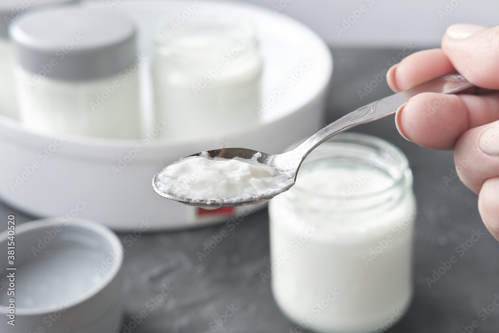 female hand holding a spoon with kefir or yogurt made in automatic yoghurt making machine. fermented dairy product for kids. children healthy meal for gut health. first meal for child. female hand holding a spoon with kefir or yogurt made in automatic yoghurt making machine. fermented dairy product for kids. children healthy meal for gut health. first meal for child.