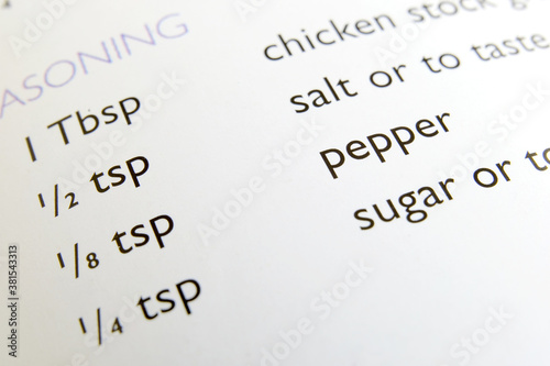 List of ingredients printed on a recipe book, closeup macro view. Page from an opened cookbook listing seasoning ingredients for a dish. Recipe showing salt, sugar to be added to enhance flavor.