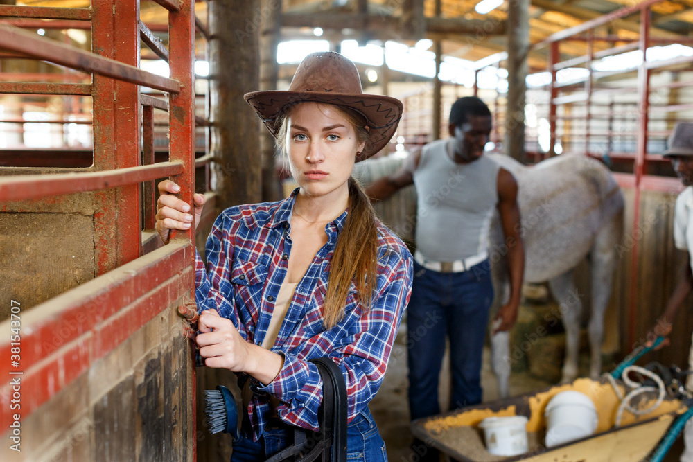 Portrait of young woman horse farm worker standing at stable