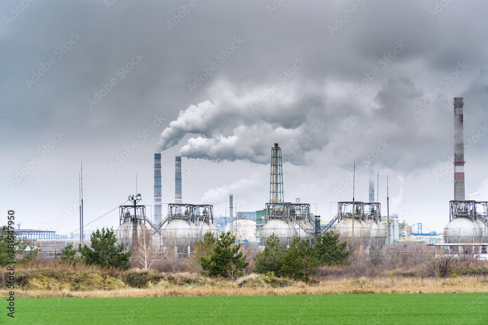 View of a chemical plant with Smoking chimneys against a dark cloudy dirty sky