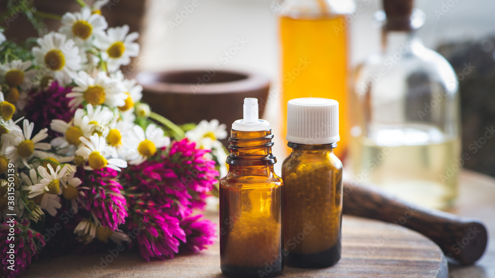 Fläschchen mit Globulis und Heilpflanzen, hier roter Klee und Kamille, im Hintergrund ein Mörser: Konzept Homöopathie Fläschchen mit Globulis und Heilpflanzen, hier roter Klee und Kamille, im Hintergrund ein Mörser: Konzept Homöopathie