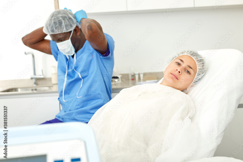 Obraz premium Female client in armchair before facial procedure in clinic of esthetic cosmetology, male on background