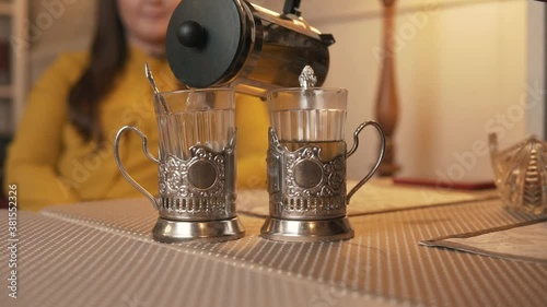 A man pours hot tea into glasses with cup holdersand spoons from a glass teapot. Tea party at the local cafe. photo