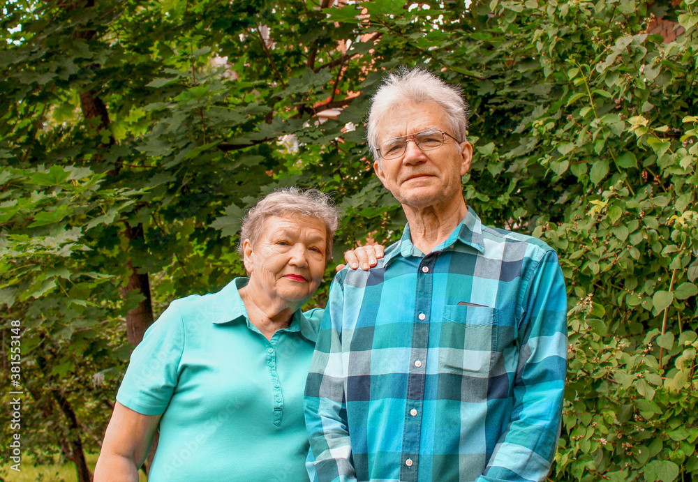 Happy elderly couple stands against a background of green foliage in the park. International Day of Older Persons and Grandparents Day Happy elderly couple stands against a background of green foliage in the park. International Day of Older Persons and Grandparents Day