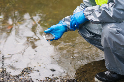 a man in a protective suit and mask took a soil sample from the bottom of the river into a Petri dish, close-up