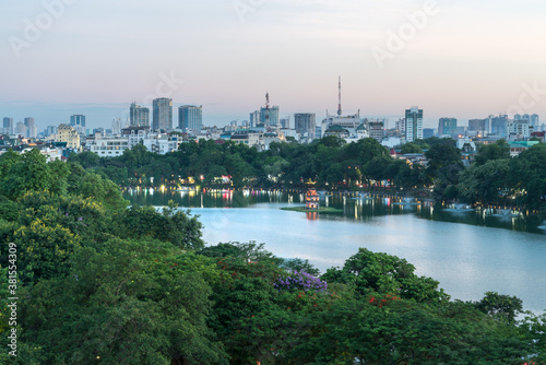 Hoan Kiem lake or Sword lake  Ho Guom in Hanoi  Vietnam with Turtle Tower  green trees and buildings on horizon  at twilight period