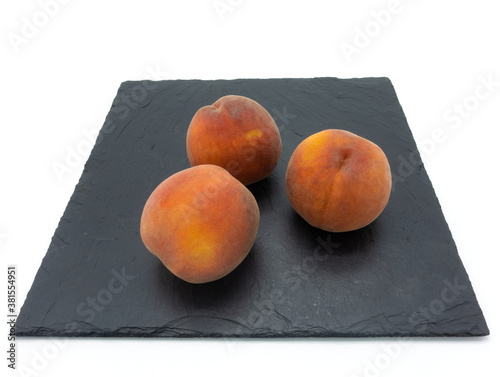 Three whole ripe peaches lie on a stone slab. Black square on a white background.