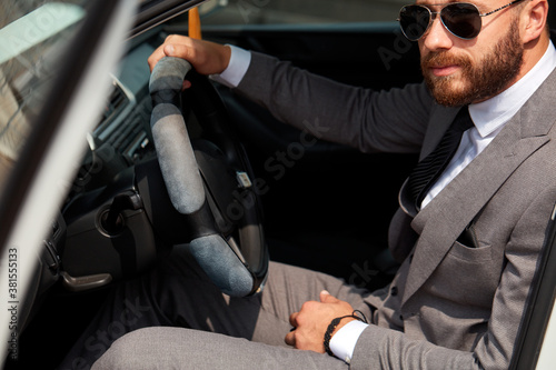 cool businessman in black sunglasses sits inside of car, drive it. successful male in formalwear, in suit. © alfa27