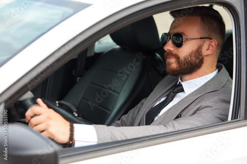 cool businessman in black sunglasses sits inside of car, drive it. successful male in formalwear, in suit.