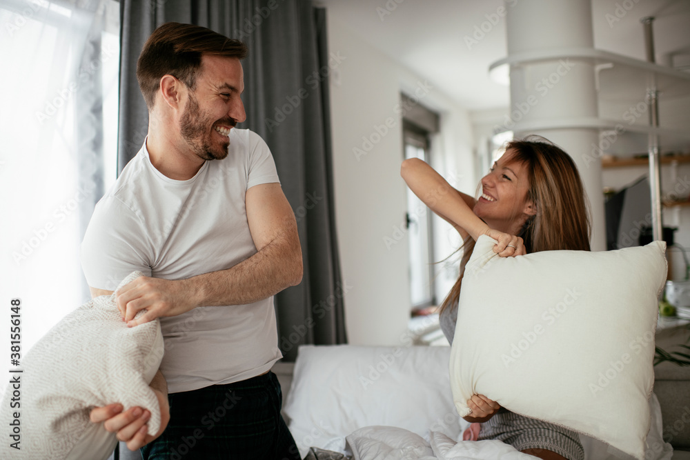 Fototapeta premium Young couple fighting pillows on the bed. Happy couple having fun at home.