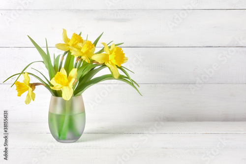 yellow daffodils at glass vase on bright wood table on white background