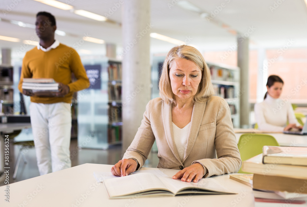 Fototapeta premium Woman with books sits at table in the library. High quality photo
