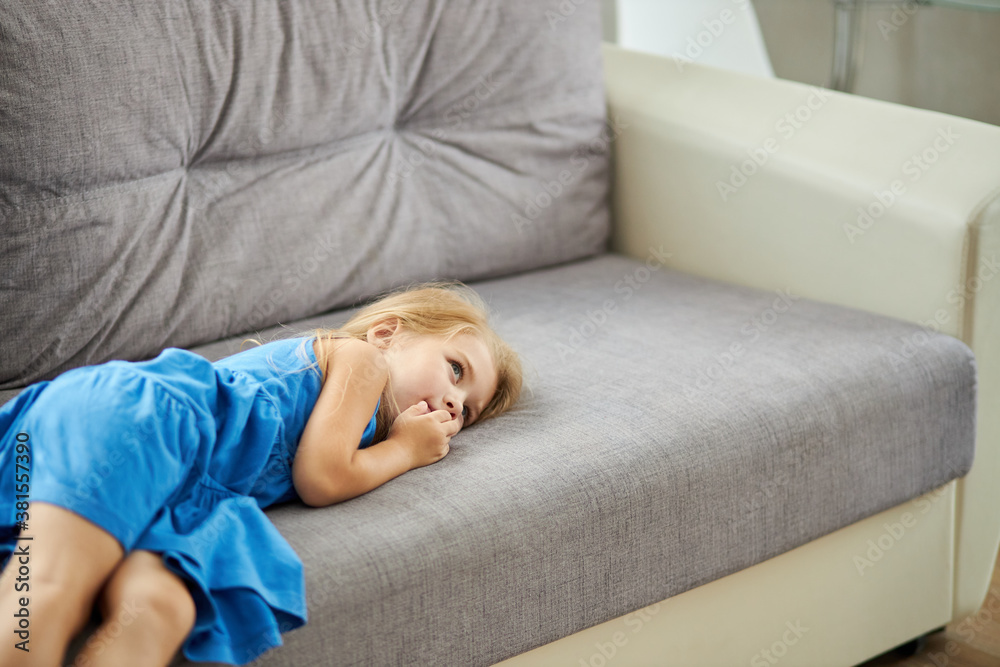 sad caucasian little girl lying on sofa alone, wearing domestic dress, depressed upset girl looking away sad caucasian little girl lying on sofa alone, wearing domestic dress, depressed upset girl looking away