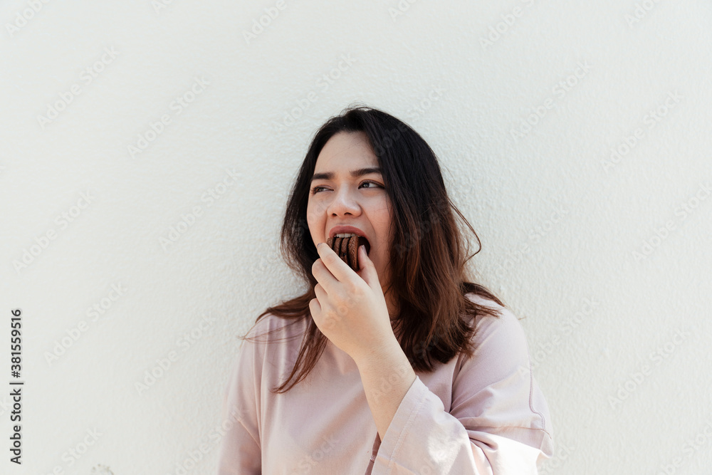 Asian chubby woman eating stack of chocolate biscuit in one bite.