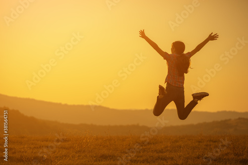 Happy teenage girl jumping in nature in sunset.