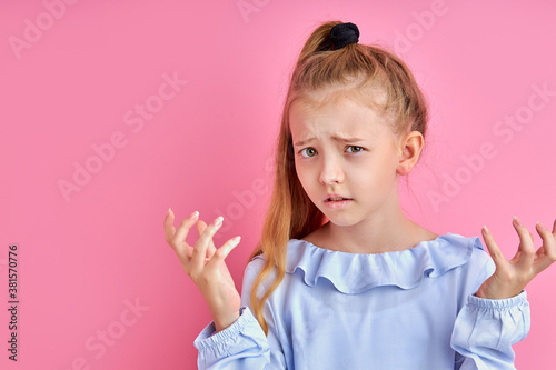 little girl is misunderstanding something, expresses unpleasantness at camera, isolated on pink background