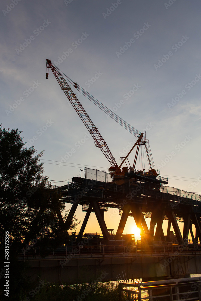 建築中の鉄橋と夕日と巨大なクレーン