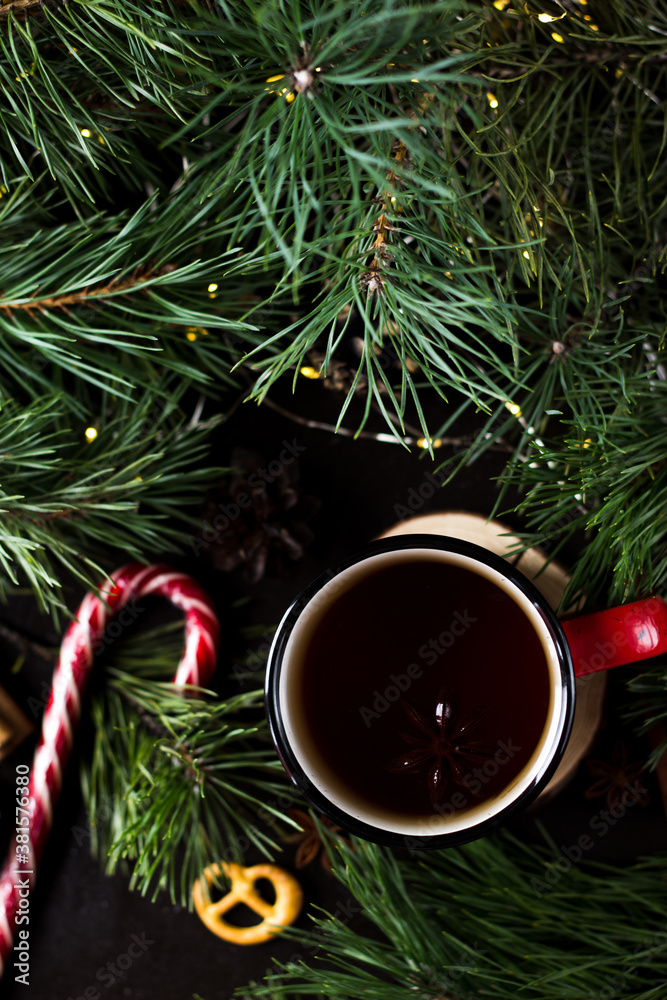 New year's tea party with spices. Red mug with tea surrounded by garlands, fir branches and spices	
