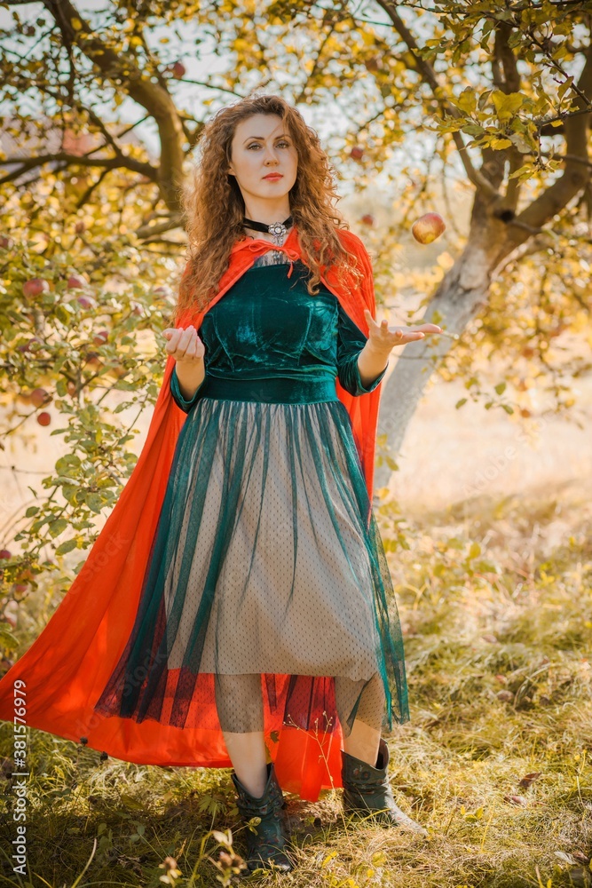 Woman in green velvet romantic dress and red hood, Halloween style for girls, autumn nature at background