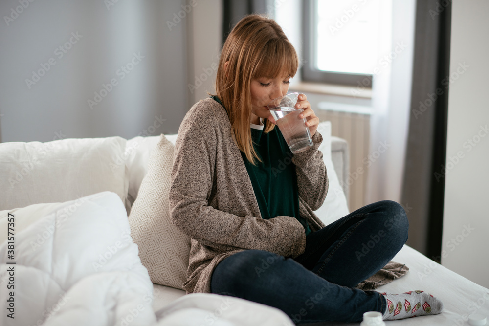 Young woman sick in bed holding glass of water.. Young woman sick in bed holding glass of water..